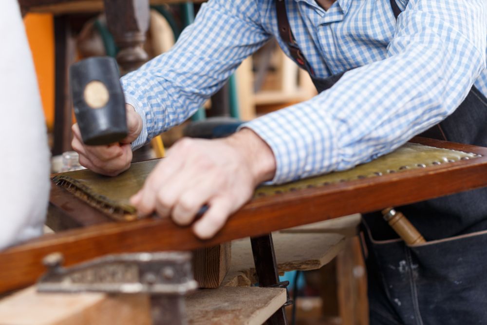 A man diligently works on a wooden chair in a workshop filled with tools and materials.
