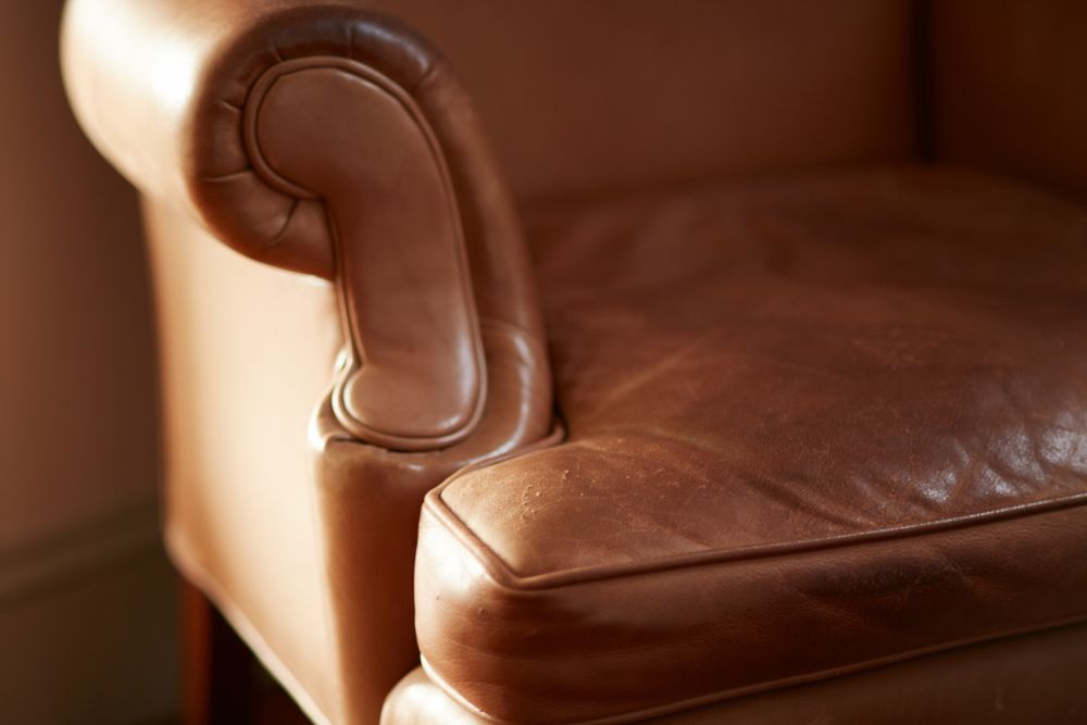 Close-up of a luxurious brown leather armchair showing its curved armrest and plush seat, highlighting its rich texture and elegant design.