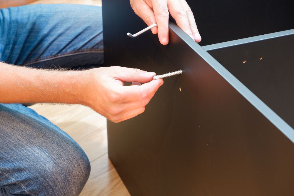A person’s hands inserting metal dowels into pre-drilled holes of a black furniture piece, preparing it for assembly.