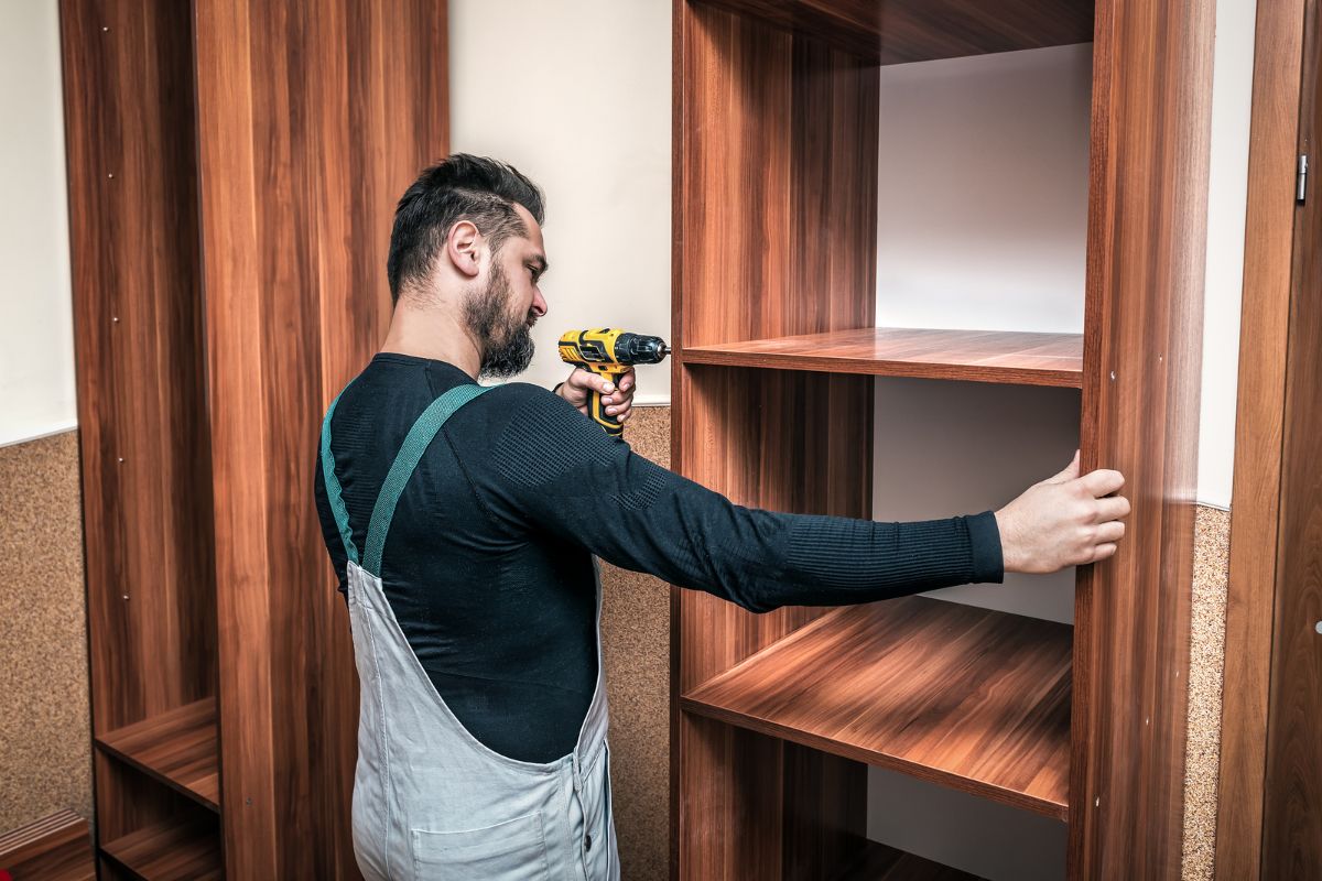 A man repairs a wooden cabinet, demonstrating skills in furniture restoration and craftsmanship.